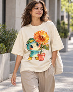 Woman on a street in an off-white oversized French terry t-shirt with a teal creature carrying a potted orange sunflower