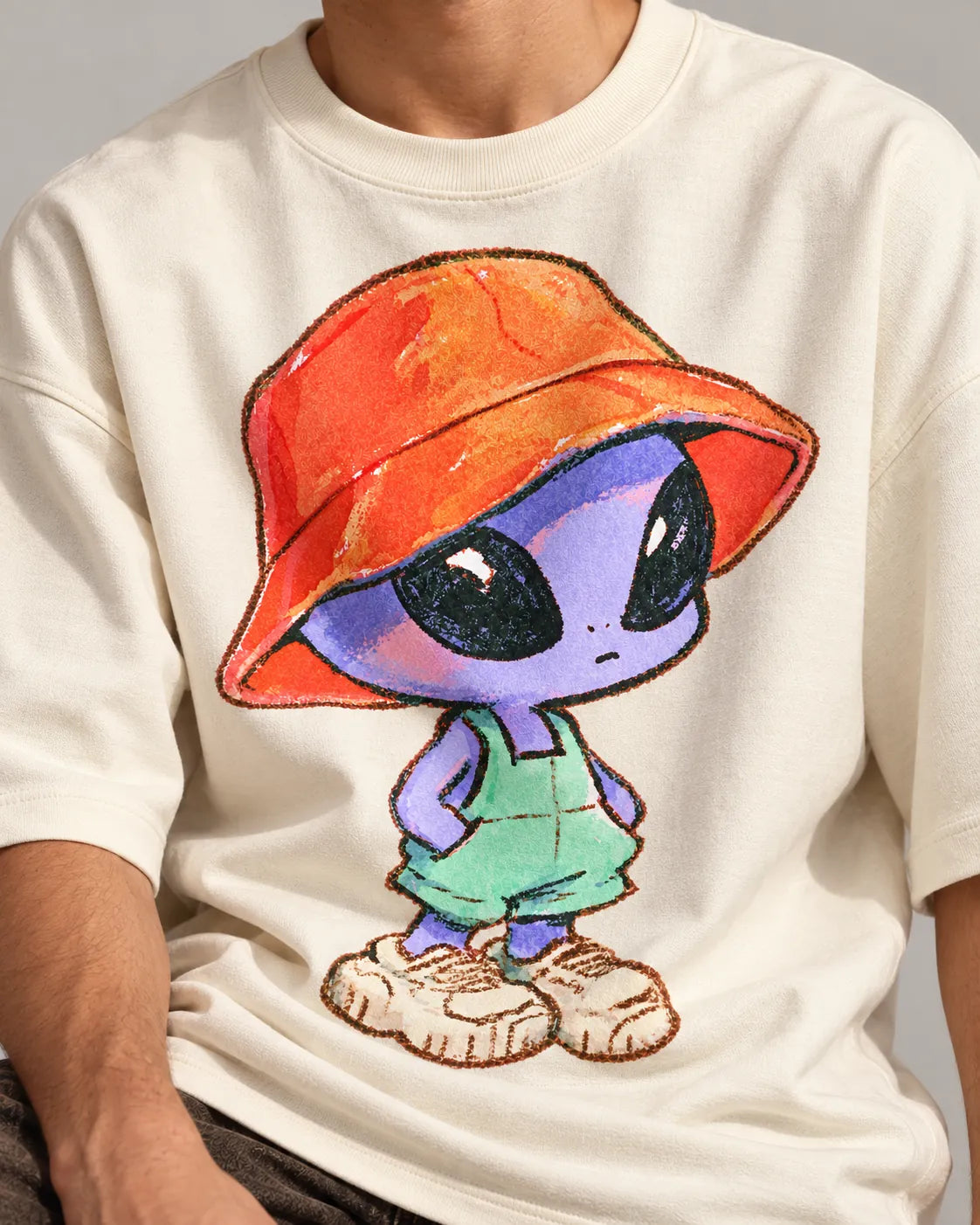 Close-up of a purple alien in a bucket hat, overalls and sneakers printed on an off-white oversized French terry t-shirt