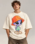 Man in an off-white oversized French terry t-shirt printed with a purple alien in a bucket hat, overalls and sneakers