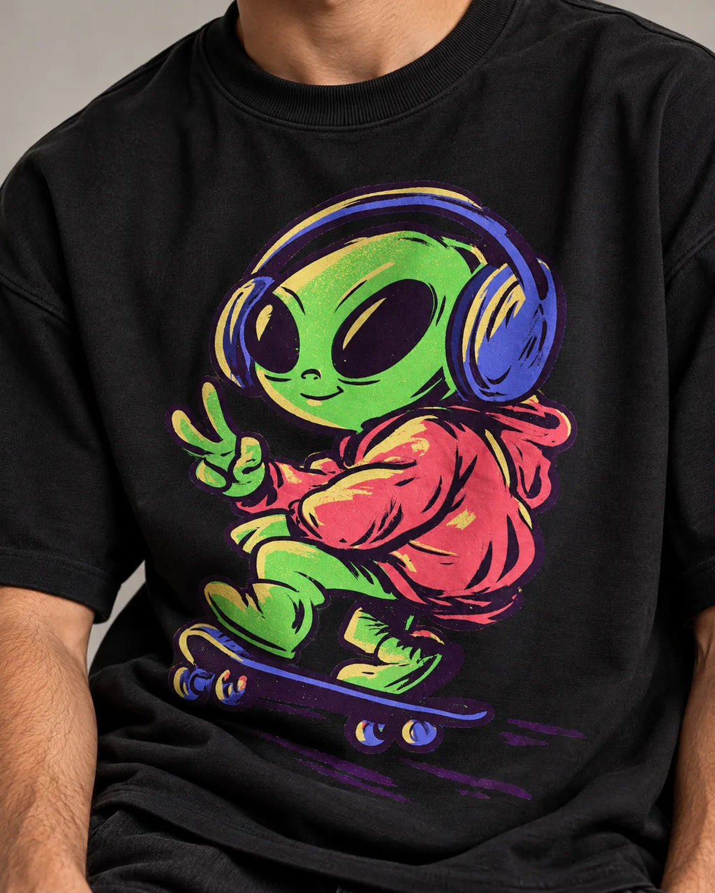 Close-up of a green alien in headphones skateboarding with a peace sign printed on a black oversized French terry t-shirt