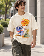 Man on a street in an off-white oversized French terry t-shirt with a blue alien in a red scarf reaching for an orange flower