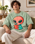 Man on a sofa in a jade oversized French terry t-shirt with a coral alien sipping a red cup through a curly straw