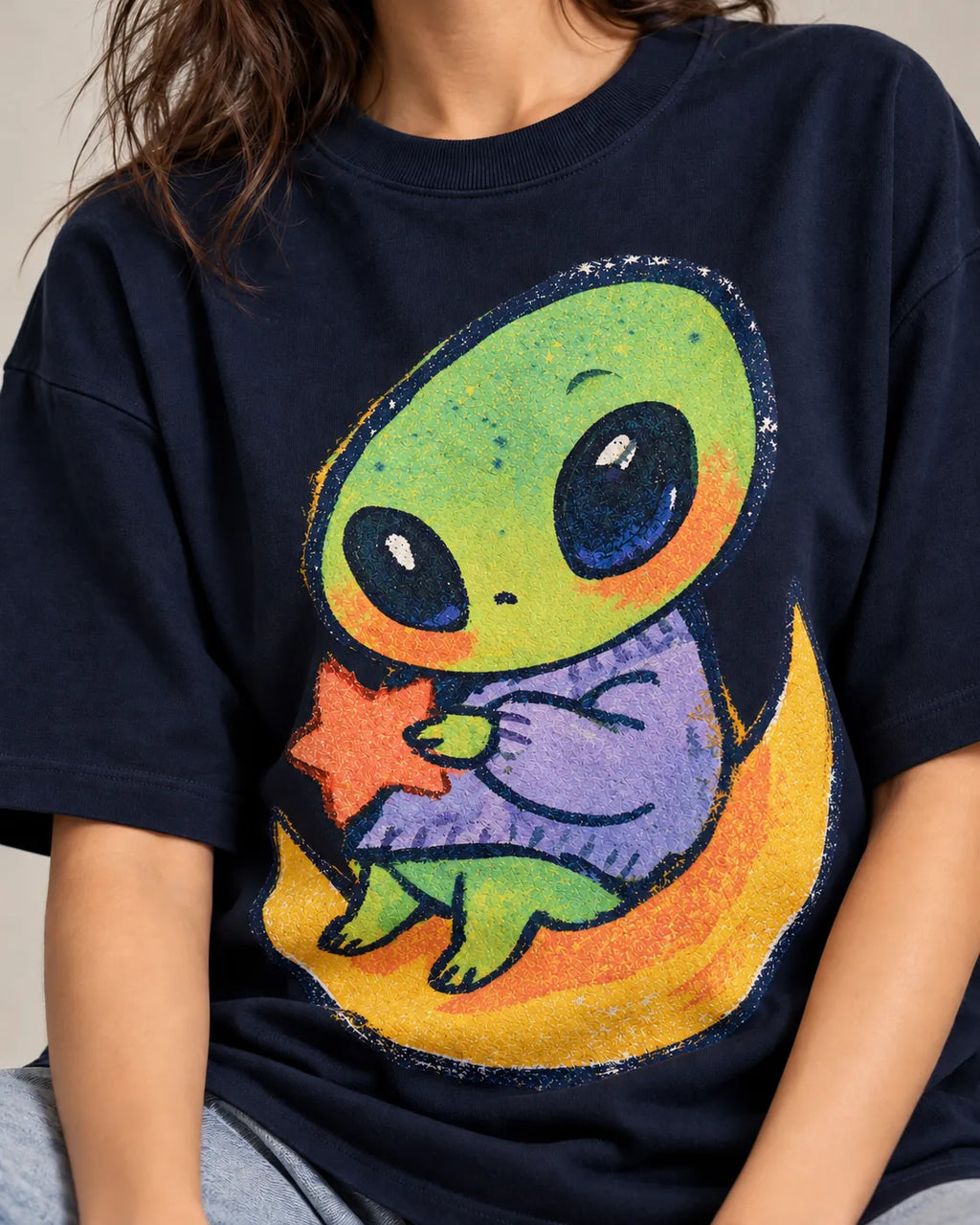 Close-up of a green alien hugging a red star on a crescent moon printed on a navy blue oversized French terry t-shirt