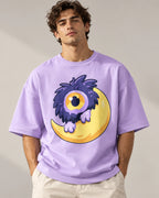 Man in a lavender oversized French terry t-shirt printed with a fluffy one-eyed purple monster on a yellow moon