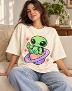Woman on a sofa in an off-white oversized French terry t-shirt with a green alien giving a thumbs-up on a ringed planet