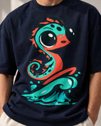 Close-up of a teal sea serpent rising from a wave printed on a navy blue oversized French terry t-shirt