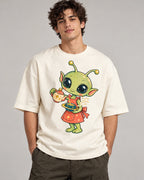 Man in an off-white oversized French terry t-shirt printed with a green alien in an apron pouring tea from a teapot