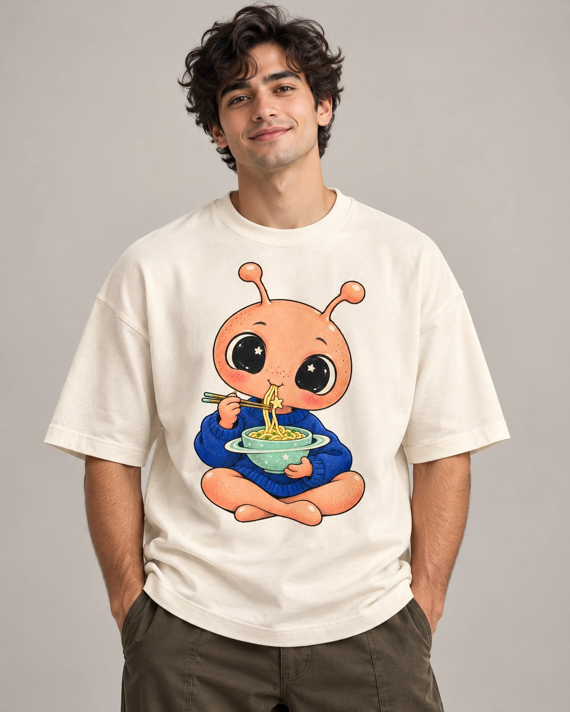 Man in an off-white oversized French terry t-shirt printed with a peach alien eating noodles from a ringed bowl