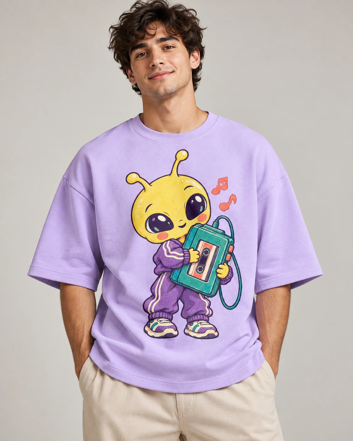 Man in a lavender oversized French terry t-shirt printed with a yellow alien in a tracksuit holding a cassette player