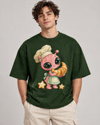 Man in a bottle green oversized French terry t-shirt printed with a pink alien chef carrying a giant croissant