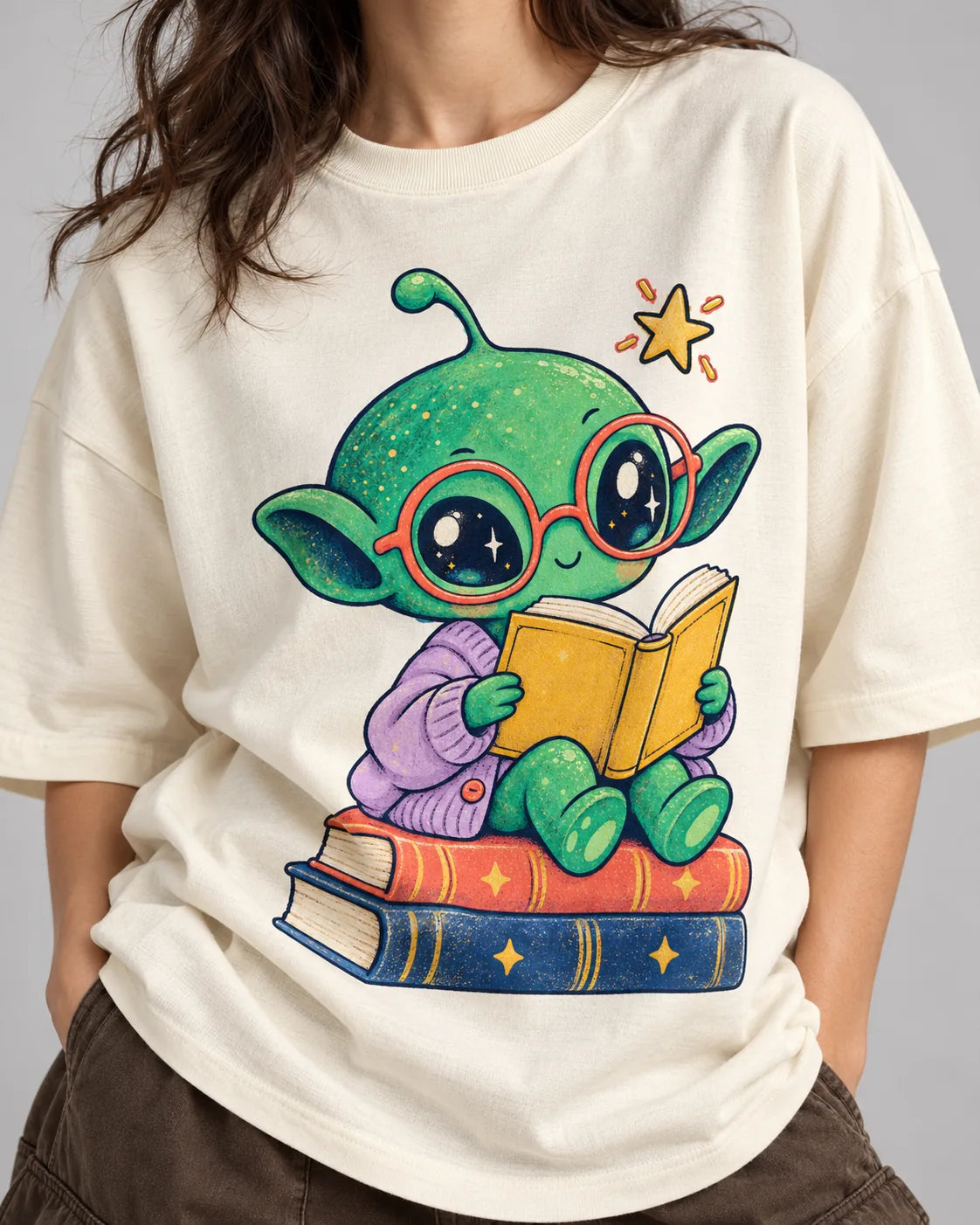 Close-up of a green alien in red glasses reading on a stack of books printed on an off-white oversized French terry t-shirt