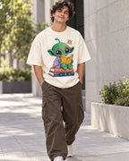 Man on a street in an off-white oversized French terry t-shirt with a green alien in red glasses reading on a stack of books