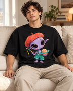 Man on a sofa in a black oversized French terry t-shirt with a purple alien in a beret painting a ringed planet