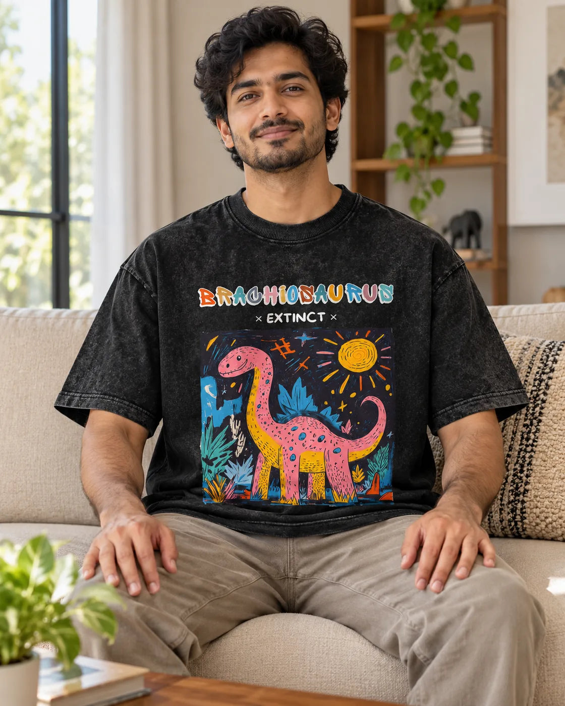 Model wearing the Brachiosaurus black acid wash oversized T-shirt seated on a sofa, Fourth Dimension Club
